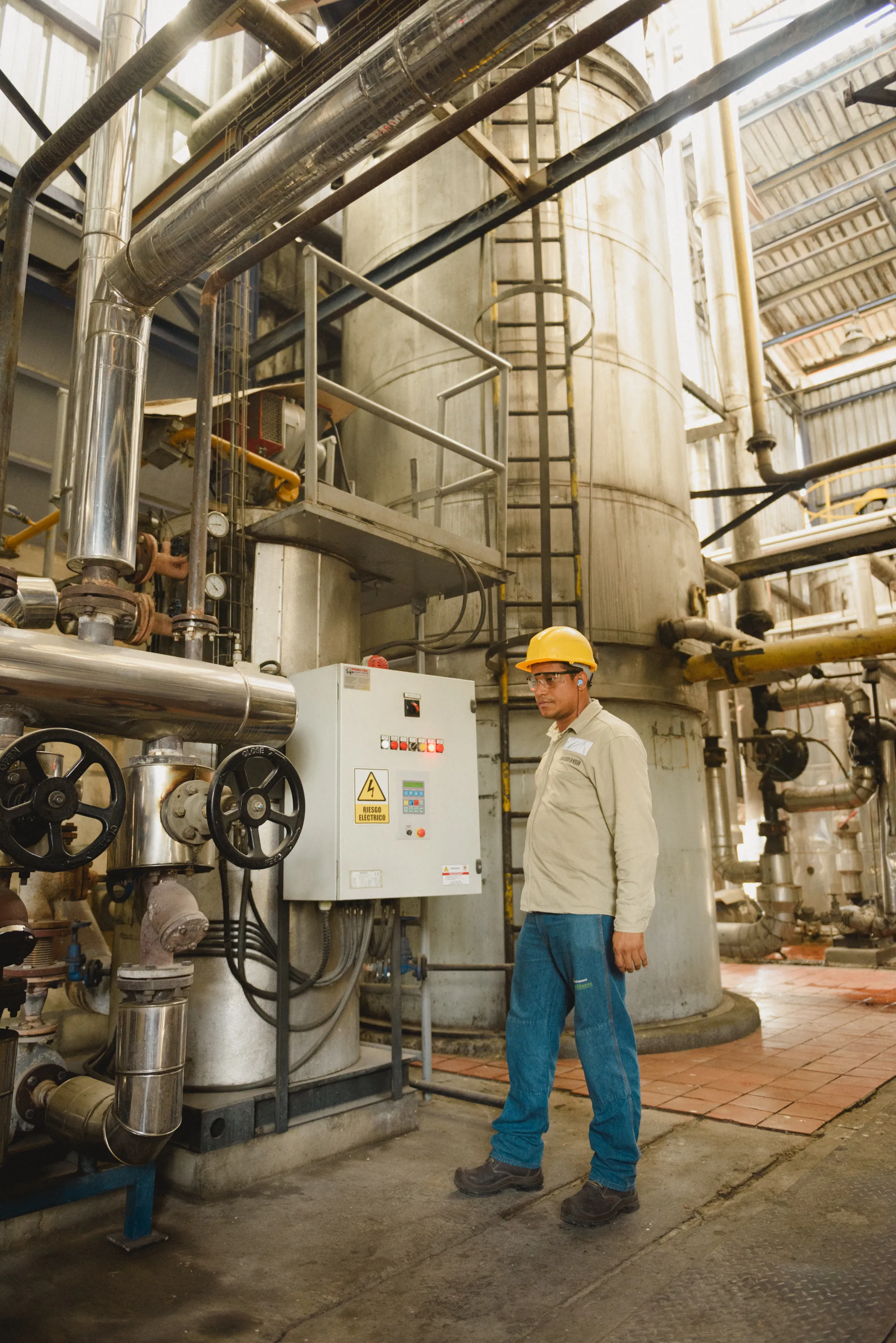 Técnico junto a equipos y tuberías de una planta de proceso.